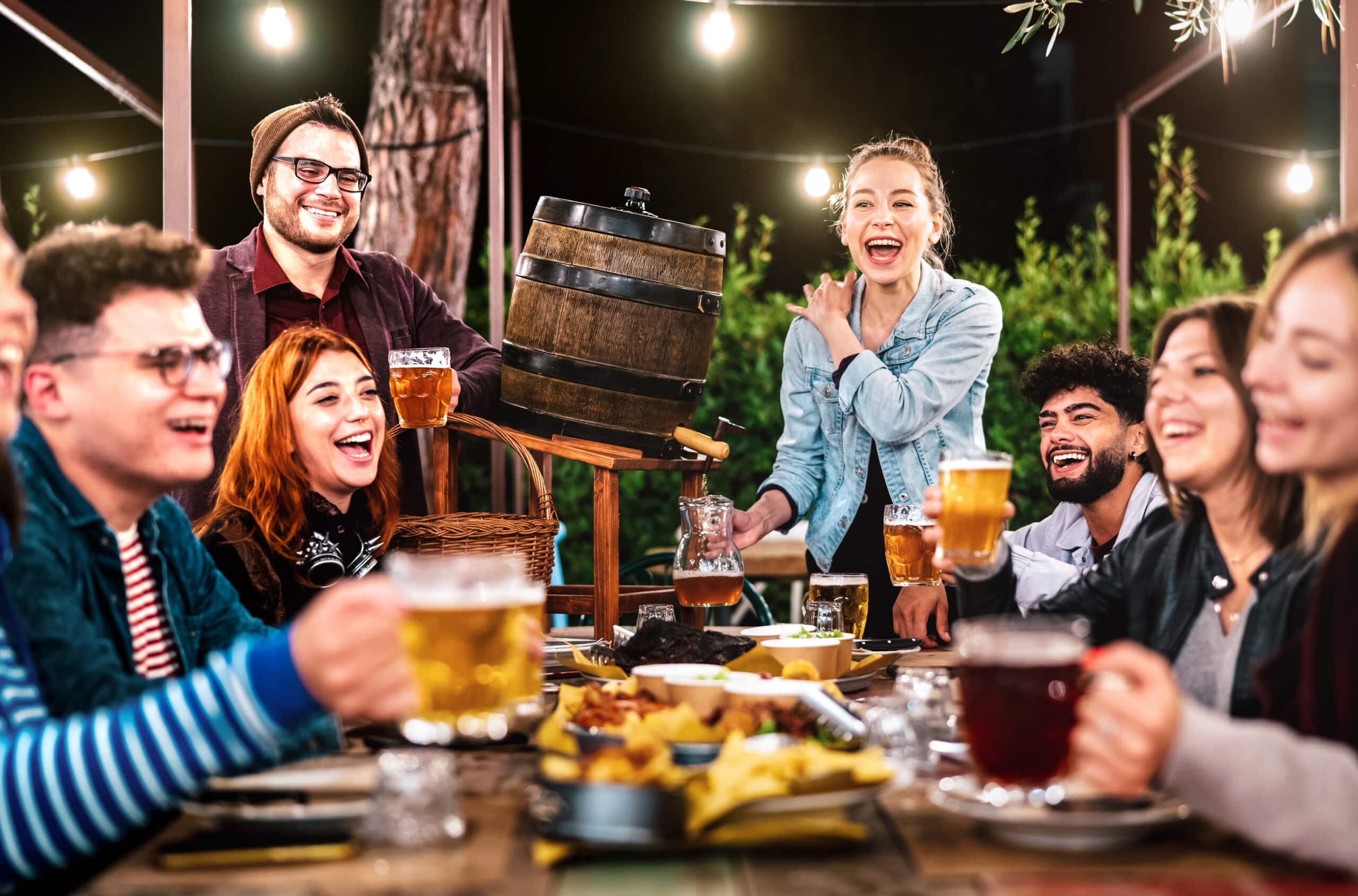 Happy men and women having fun drinking out at beer garden - Social gathering life style concept on young people enjoying hangout time together at night - Warm filter with shallow depth of field