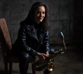 Vanessa Collier sits on a chair holding a saxophone.
